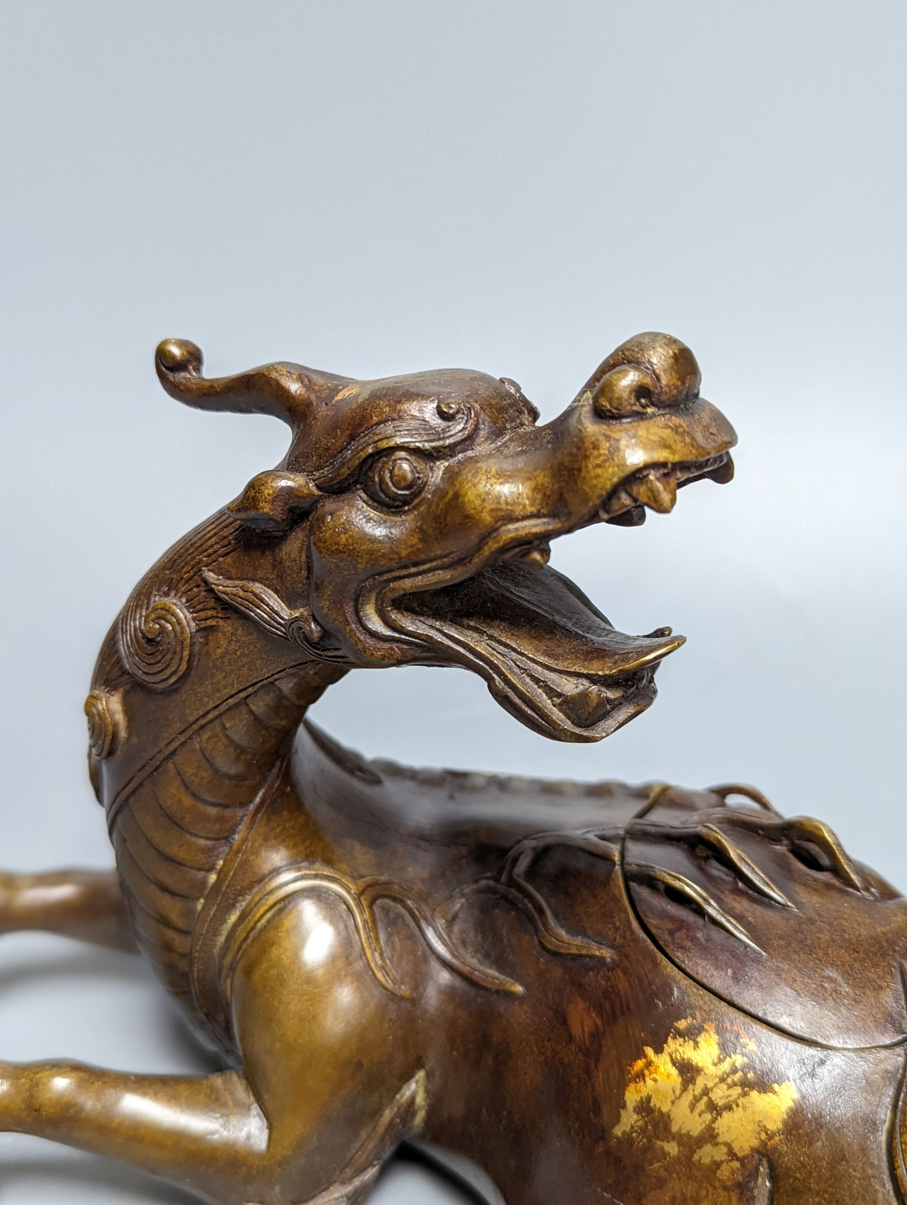 A Chinese parcel-gilt bronze incense burner and cover, modelled as a recumbent qilin, Qing dynasty, 19th century, 25 cms wide.